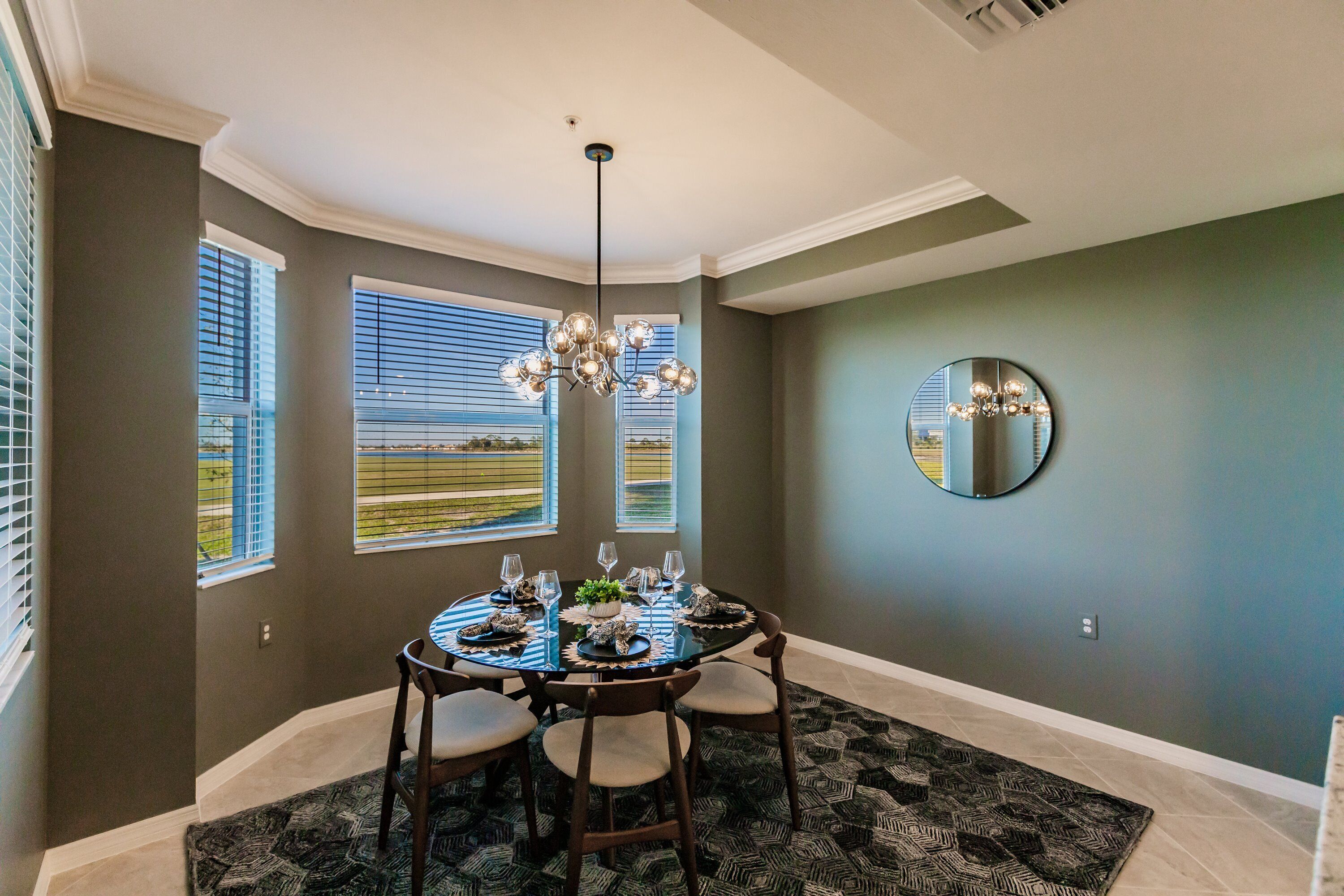 A dining area with a round table set for four, a chandelier, and a large mirror on the wall.