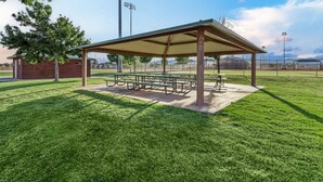A covered picnic area with benches and tables, surrounded by a well-maintained lawn and a sports field in the background. - Paradise Retreat 94 & 96 | Neighboring Homes, Kid Friendly w/ Hot Tub's, Private Pool, Game Stations (Santa Clara)