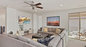 A modern living room with a sectional sofa, a flat-screen TV, and a ceiling fan.