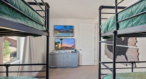 A room with bunk beds, a desk with a computer, and a TV on the wall.