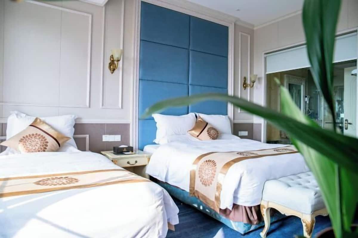 Habitación de hotel con dos camas, un ventanal grande y una pared azul.