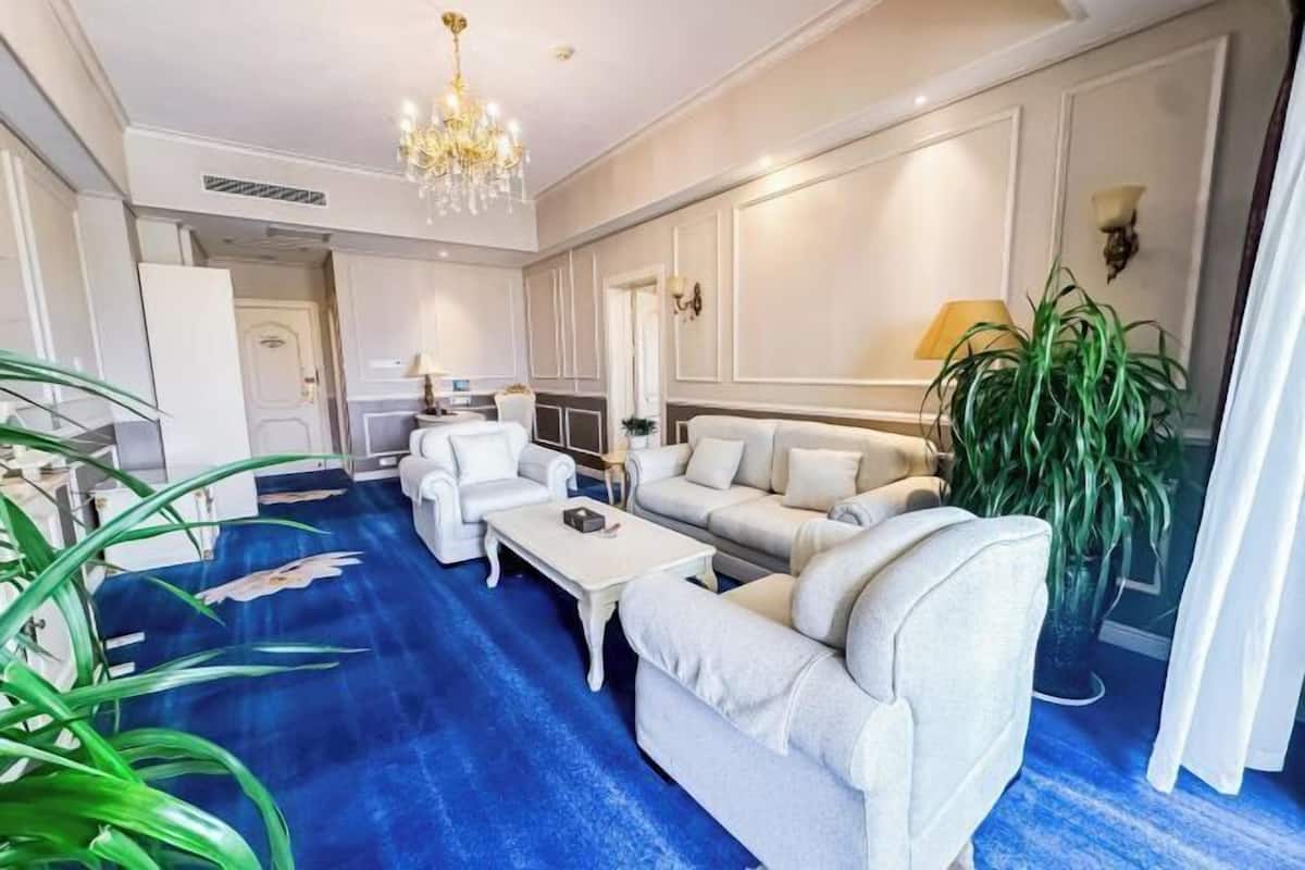 Un salón amplio con alfombra azul, sofás blancos, una mesa de centro y una lámpara de araña.