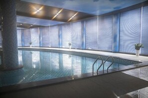 An indoor swimming pool with clear water, surrounded by walls with a wavy pattern, and a ceiling with recessed lighting. - Jintian International Hotel (Suqian)