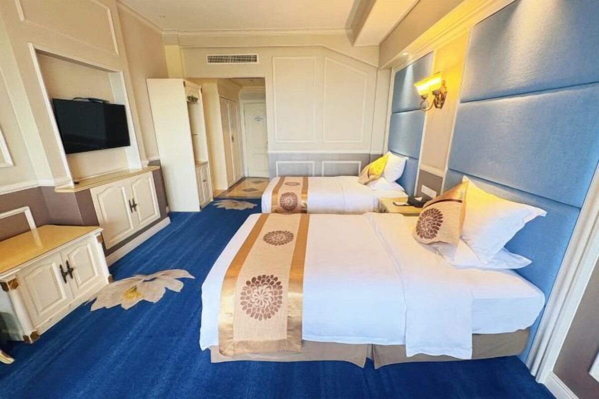 A hotel room with two beds, a TV, a desk, and a large mirror.