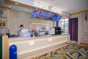 Una zona de cafetería con una pantalla digital de menú, una barra con un tablero de menú y un basurero.