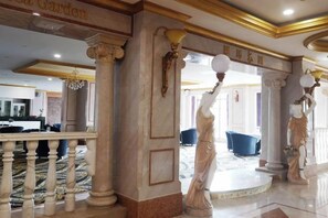 A grand lobby with marble columns, a central fountain, and a reception area in the background.