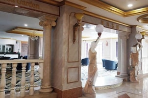 A grand lobby with marble columns, a central fountain, and a reception area in the background.
