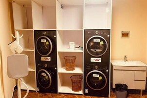 A laundry room with multiple washing machines, a sink, and a trash bin.