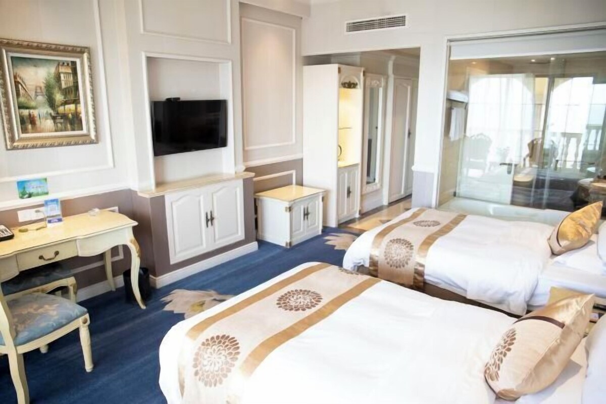 A hotel room with two beds, a desk, a chair, a television, and a large window.
