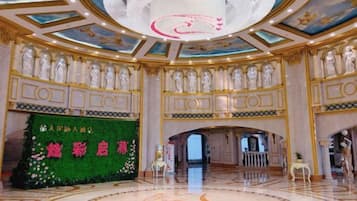 Um amplo saguão de hotel com piso de mármore circular, um lustre imponente e um painel floral verde com caracteres chineses.