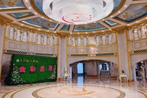 Un amplio vestíbulo de hotel con piso de mármol circular, una gran lámpara de araña y un fondo floral verde con caracteres chinos.