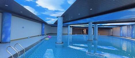 A large indoor swimming pool with clear blue water, surrounded by walls and a ceiling with a grid pattern.