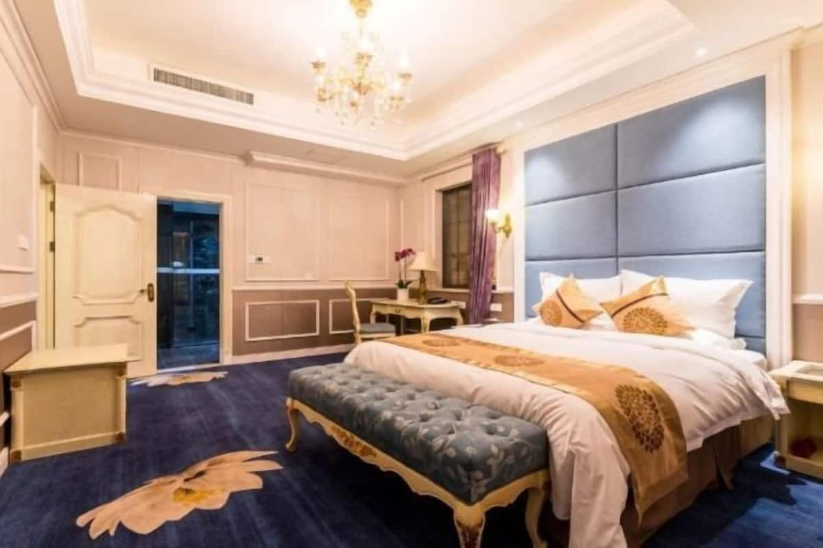 Un dormitorio amplio con una cama grande, un banco tapizado, un escritorio y una araña.