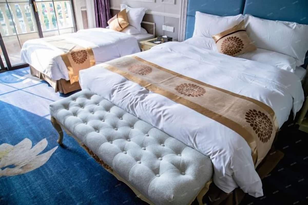 Una habitación de hotel con dos camas, un amplio banco acolchado y una alfombra azul con estampado floral.