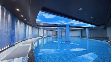An indoor swimming pool with a curved design, a ceiling with a sky-like pattern, and a tiled floor.