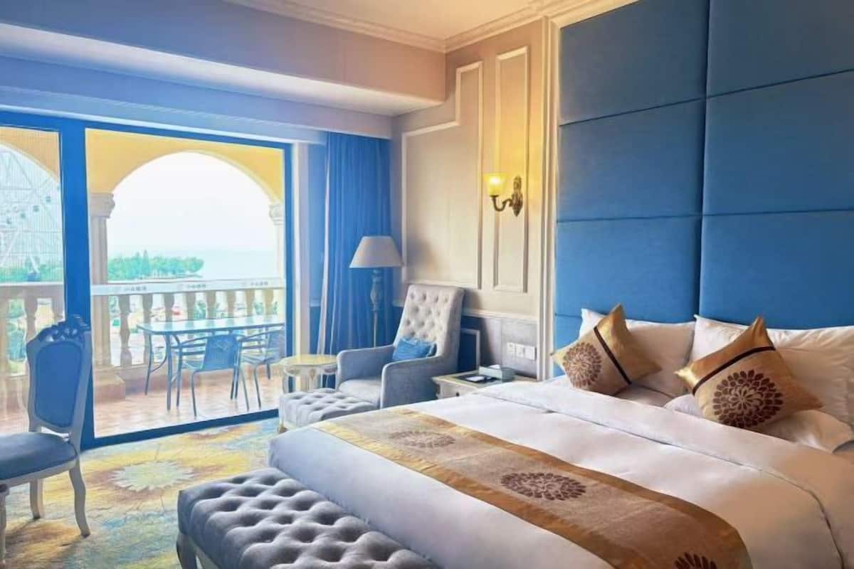 Habitación de hotel con una cama grande, un balcón con vistas, una zona de estar y un candelabro.