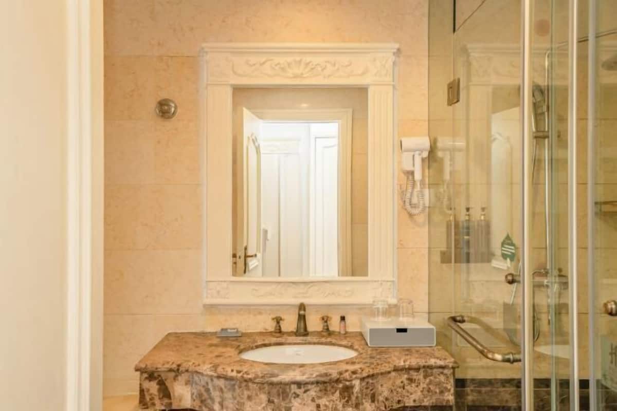 Un baño con lavamanos de mármol, un espejo grande y una cabina de ducha con paredes de vidrio.