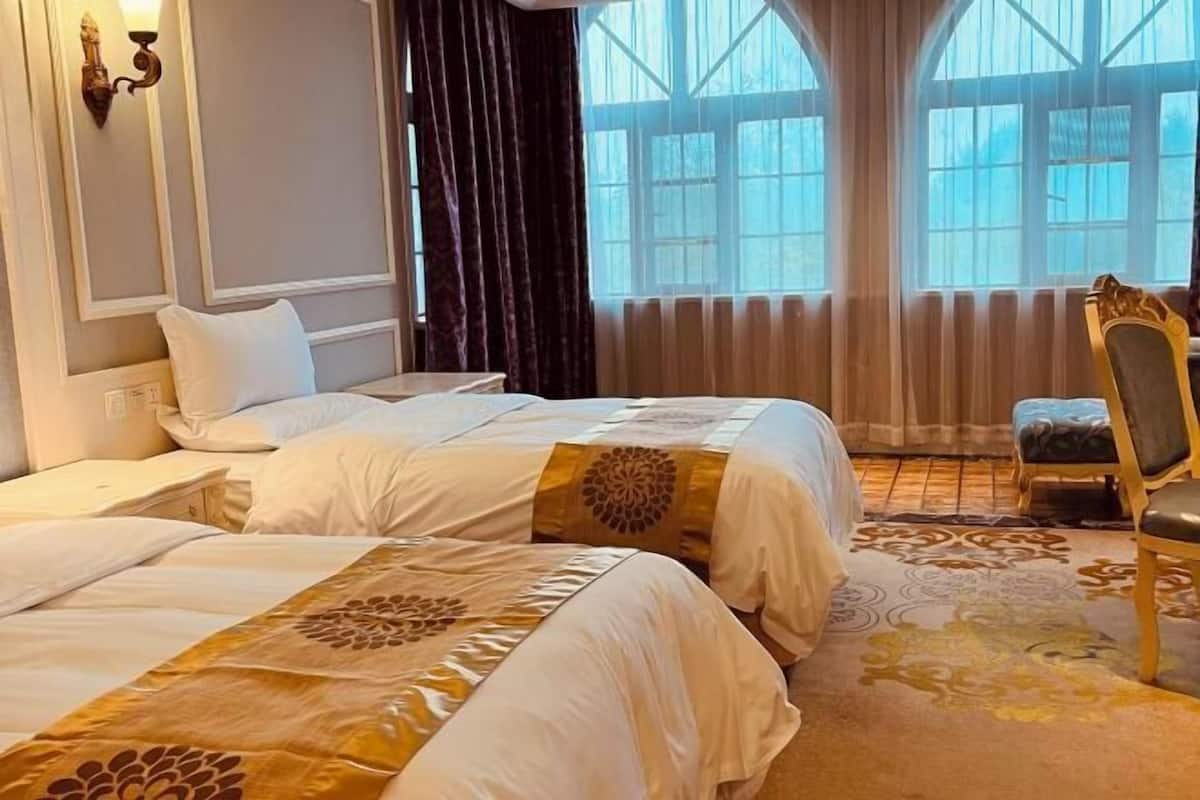 Habitación de hotel con dos camas, una silla y ventanas amplias.