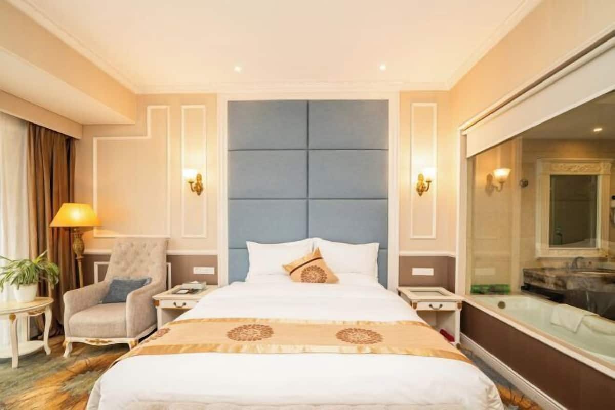 Habitación de hotel con una cama grande, una silla, una mesita de noche, una lámpara y un baño con bañera.