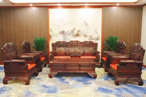 A room with a large wooden sofa set, two armchairs, and a matching coffee table. - Jintian International Hotel (Suqian)