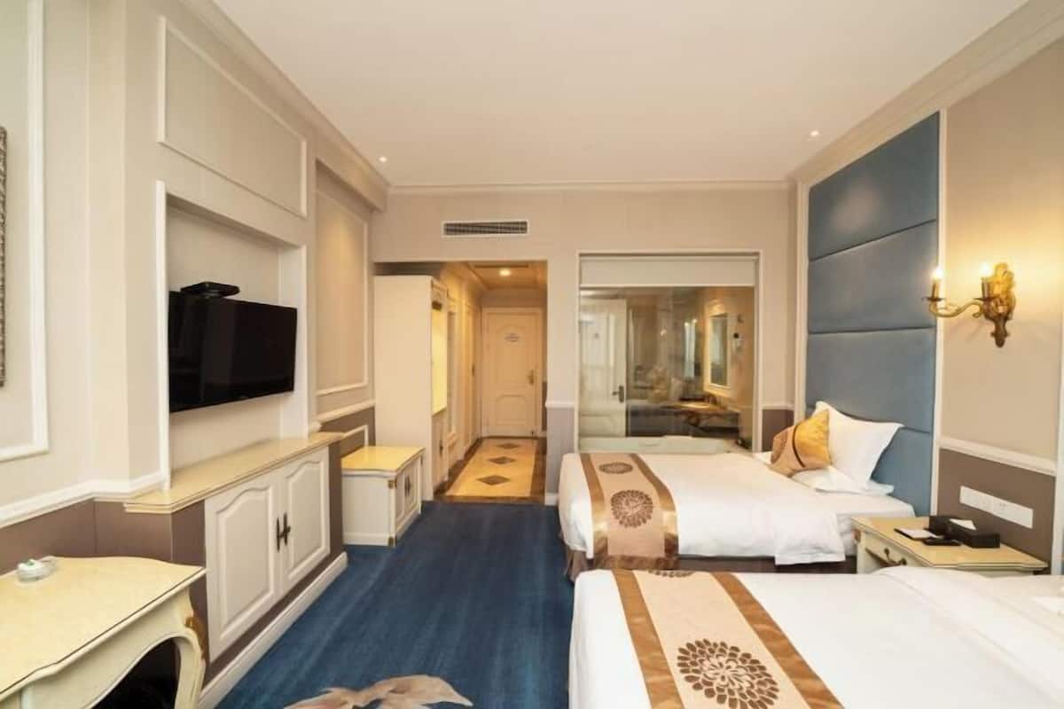 Habitación de hotel con dos camas, televisión, escritorio y espejo.