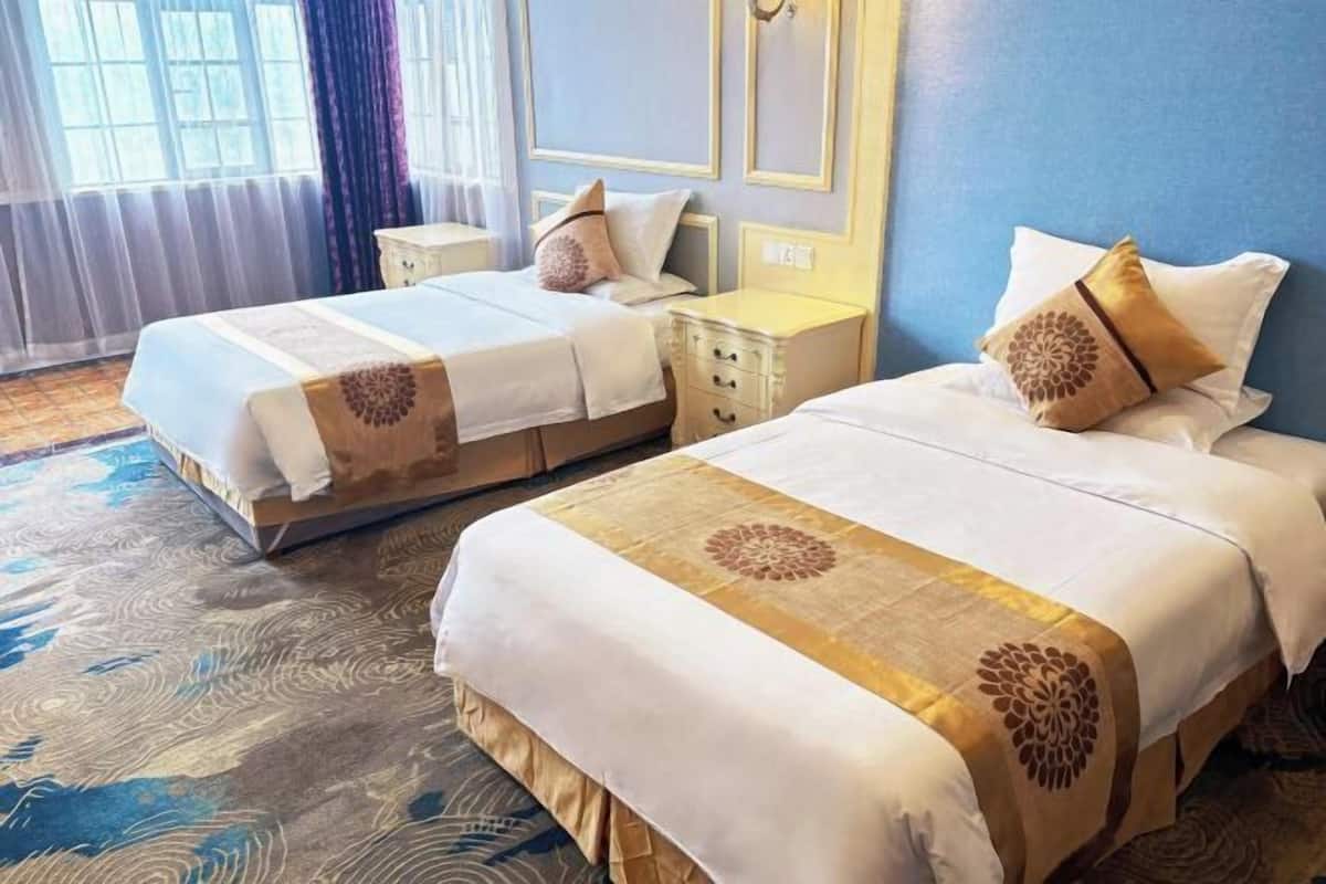Habitación de hotel con dos camas, una mesita de noche, un aparador y un amplio ventanal con cortinas.
