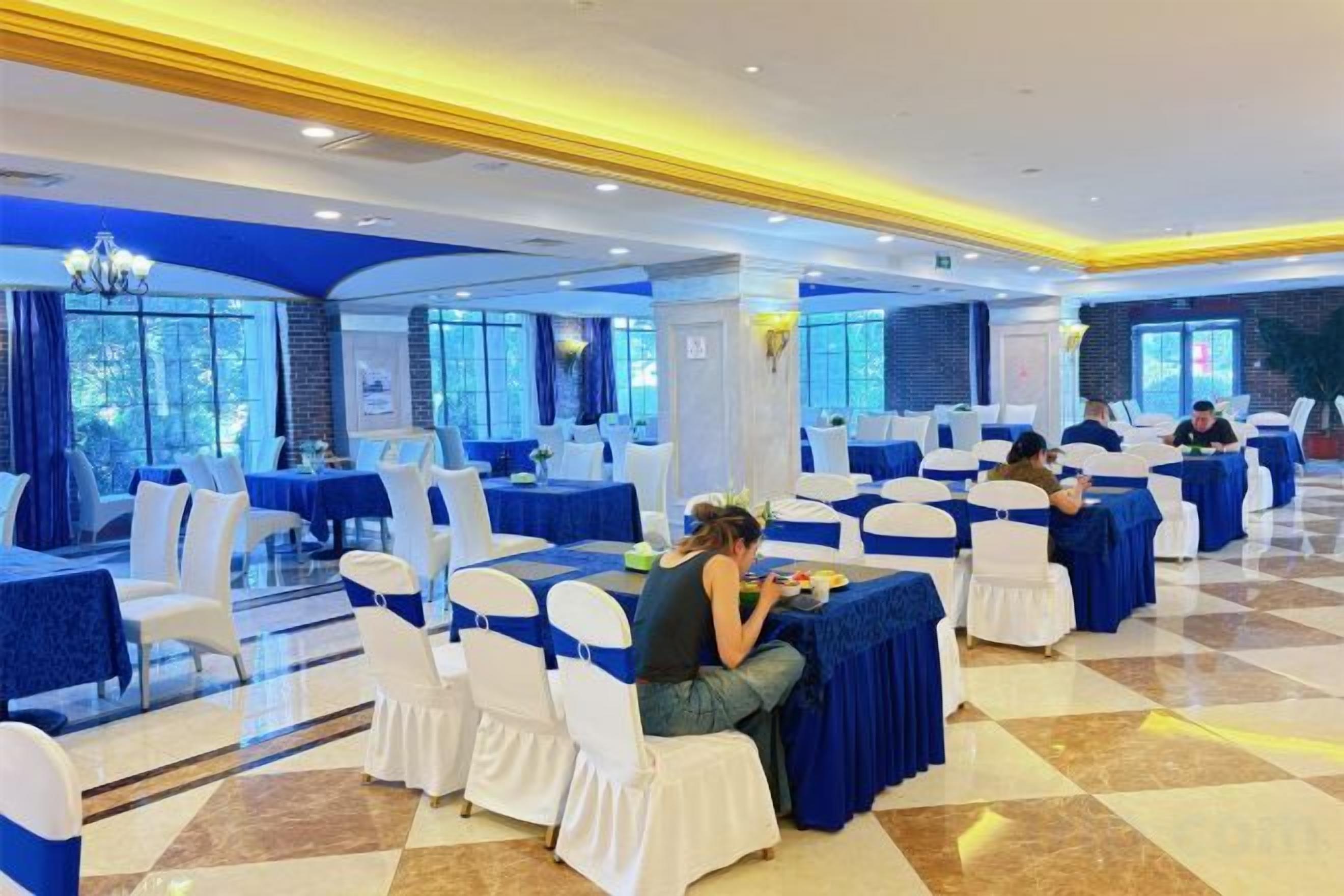 A banquet hall with round tables, white chairs, and blue tablecloths.