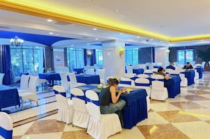 Un salón de banquetes con mesas redondas, sillas blancas y manteles azules.