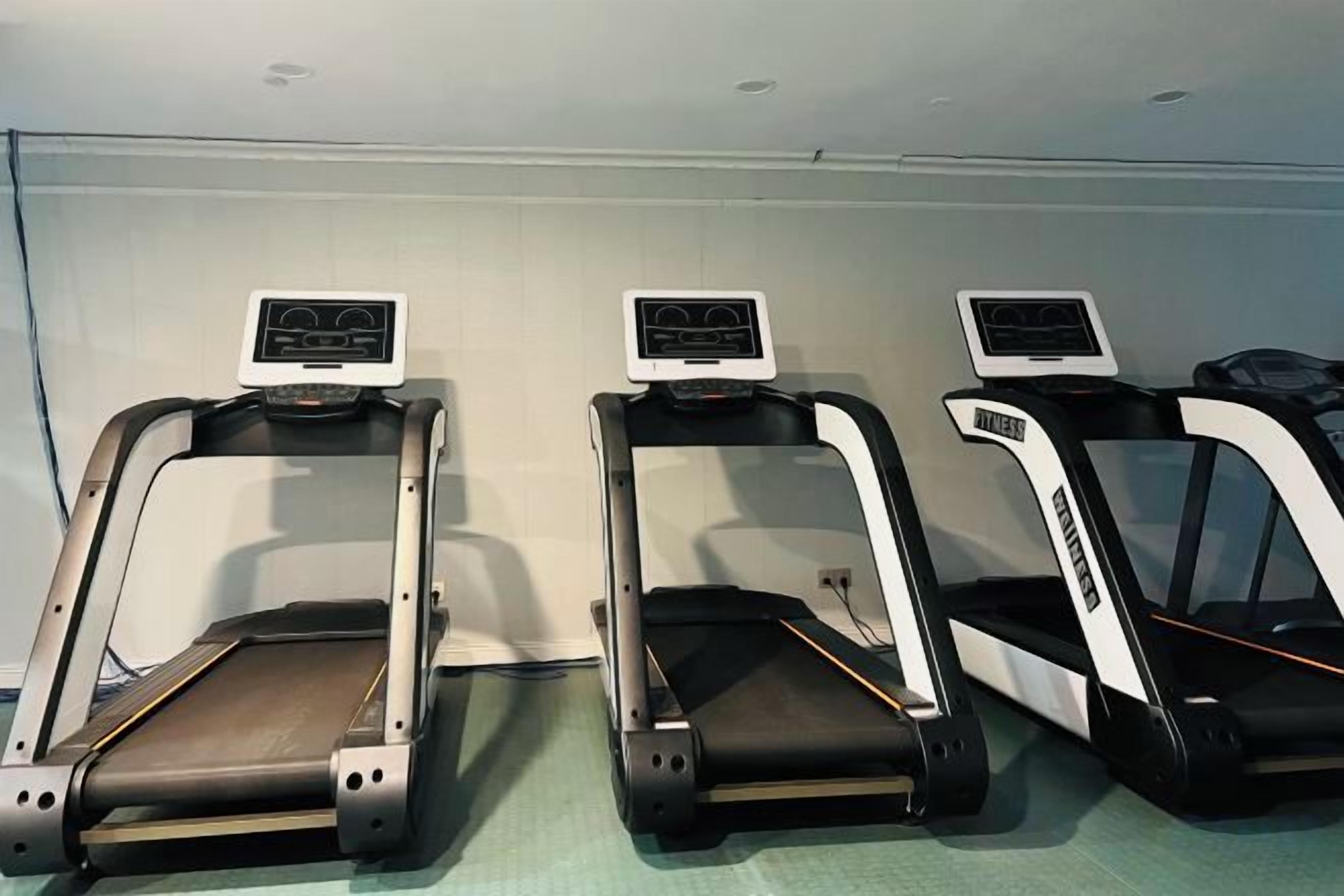 Three treadmills aligned against a wall in a room with a tiled floor.