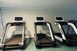 Three treadmills aligned against a wall in a room with a tiled floor.