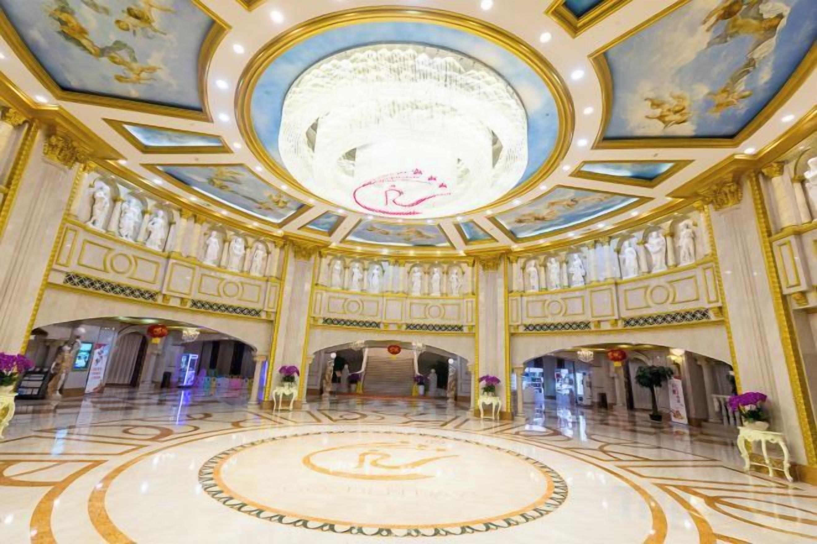 A grand lobby with a circular floor design, a large chandelier, and classical statues.