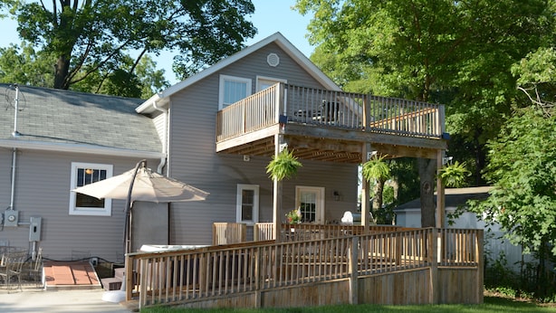 Ein zweistöckiges Haus mit Balkon, überdachter Terrasse und kleiner Holzterrasse.