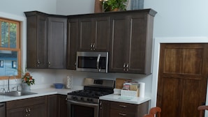 Eine Küche mit dunklen Holzausführungen, Edelstahlgeräten, einem Deckenventilator und einem Essbereich mit Holztischen und einer Tischplatte.