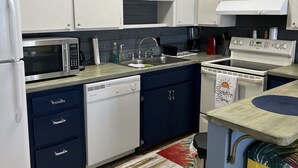 Een keuken met witte kastjes, een magnetron, een spoelbak en een fornuis.