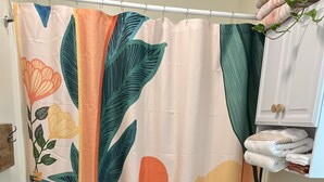 Een badkamer met een douchegordijn met tropische bladmotieven, een toilet en een wastafel met een wit aanrecht.
