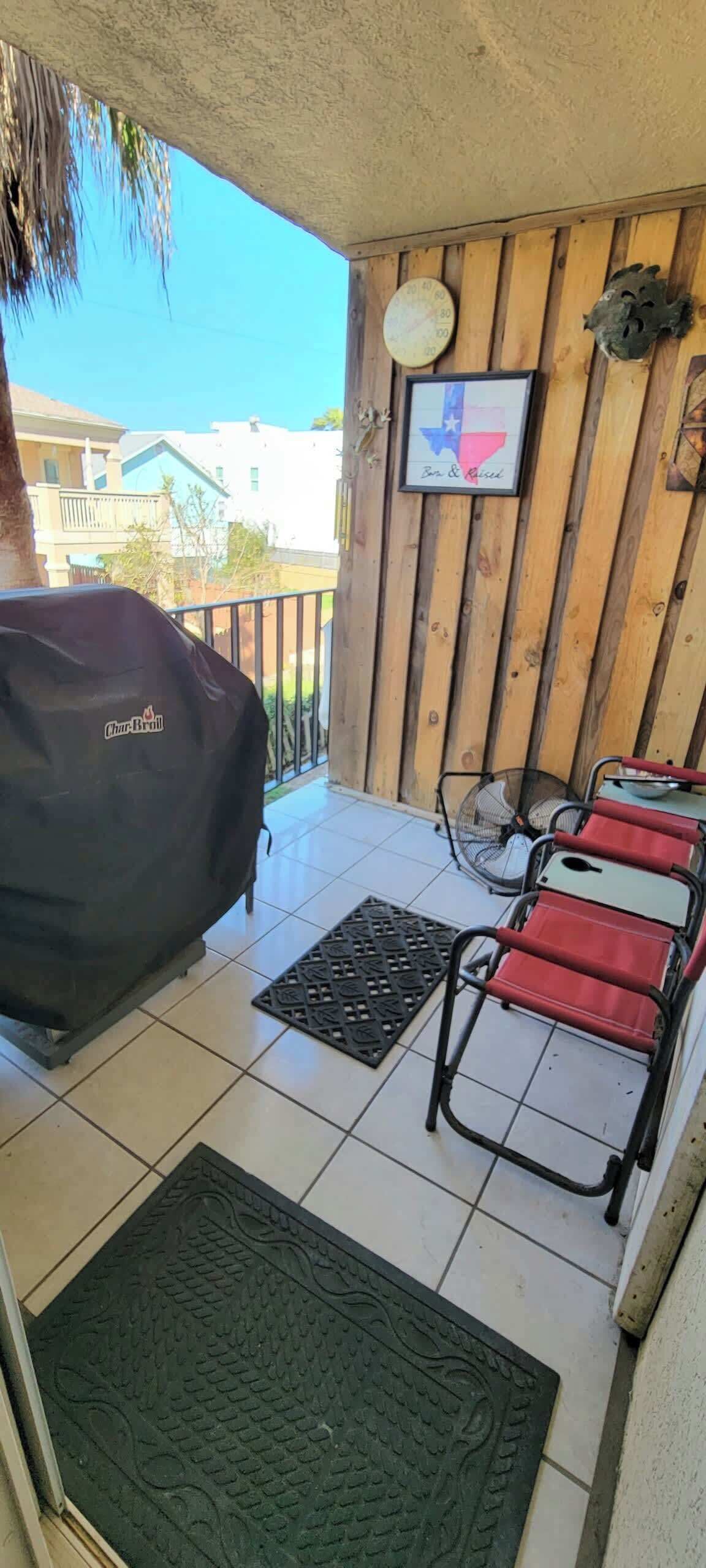 A covered patio area with a barbecue grill, red chairs, a Texas flag, and a thermometer on the wall.