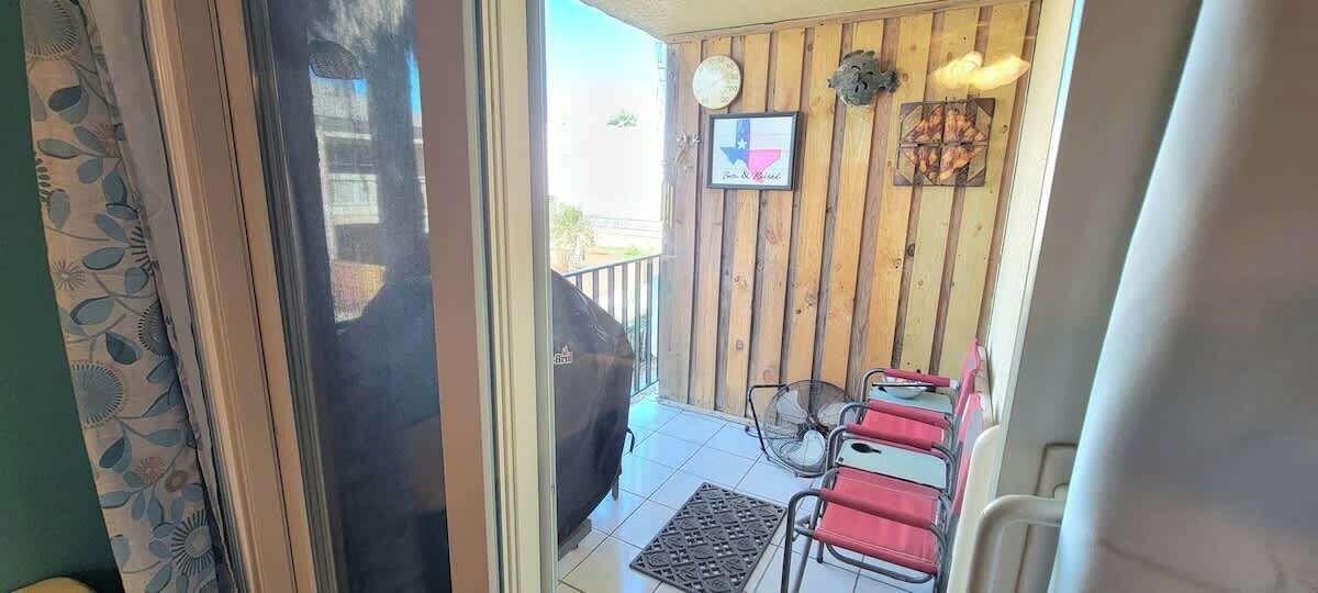 A balcony with a barbecue grill, two red chairs, and a small table.