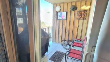 A balcony with a barbecue grill, two red chairs, and a small table.
