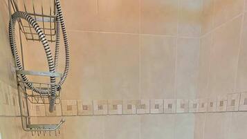 Une petite salle de douche carrelée, équipée d’un pommeau de douche à main, d’une étagère en métal et d’un drain.