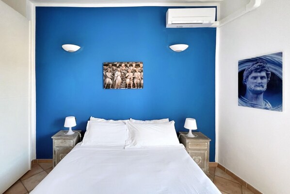 A bedroom with a blue accent wall, a bed with white linens, two bedside tables with lamps, and a framed picture above the bed.