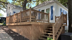 A wooden deck with a staircase leading to a white building with blue shutters.