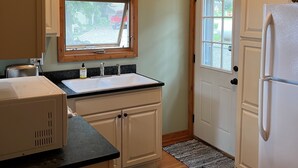 A compact kitchen with a wooden ceiling, a window, a sink, a refrigerator, and a door.