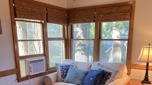 A cozy room with a beige sofa, a grey rug, wooden floors, and large windows with blinds.