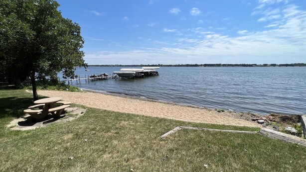 A lakeside picnic area with a table and benches, a dock with boats, and a clear sky.