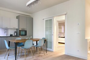 Eine moderne Küche mit Essbereich, ausgestattet mit einem Holztisch und hellblauen Stühlen, einer Kandelaber und einer Glastür, die in einen anderen Raum führt.