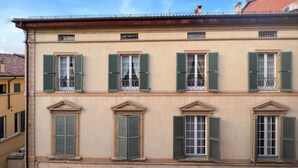 A building with multiple windows, each with green shutters, and a series of arches below the windows. - UR-NEST San Giorgio - gorgeous flat (Bologna)