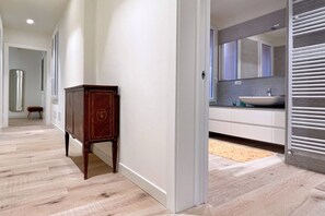 Een gang met een houten kast, een witte deur en een badkamer met een wastafel en spiegel.