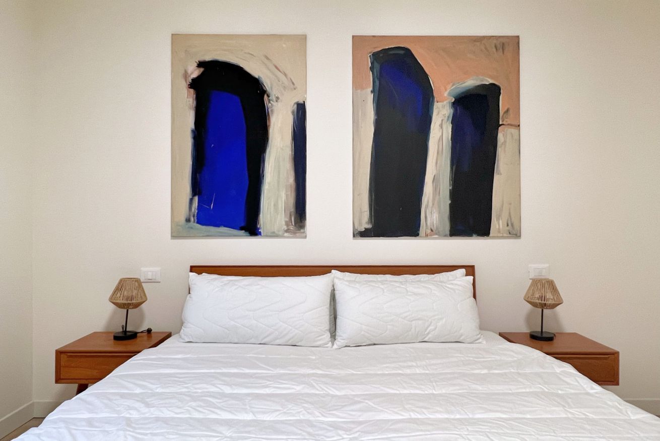 A hotel room with a large bed, two nightstands, and two abstract paintings on the wall.