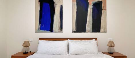 A hotel room with a large bed, two nightstands, and two abstract paintings on the wall.