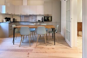 Een moderne keuken met witte kastjes, een houten eettafel en lichtgrijze stoelen.